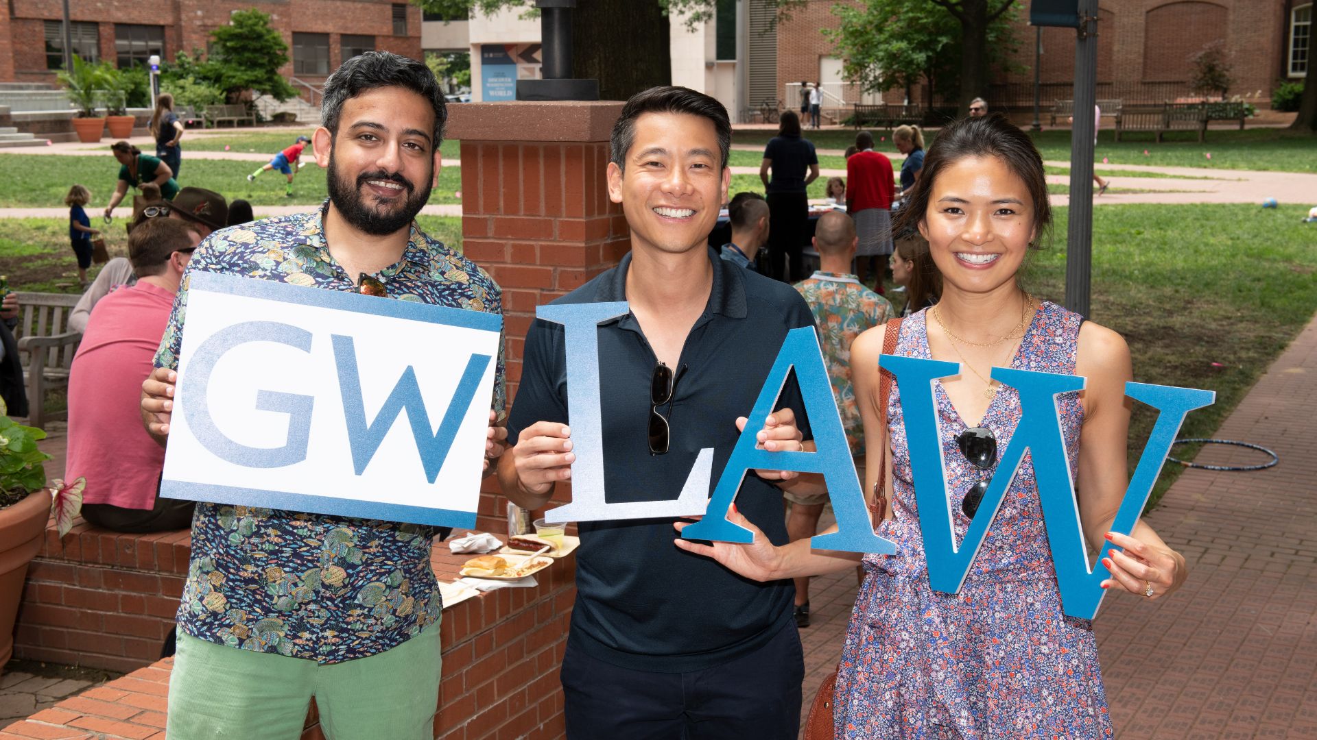 Alumni at reunion weekend two men one woman holding GW LAW sign up