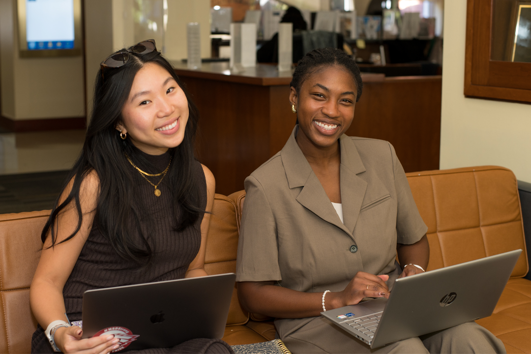 Two female students on their laptops smiling at the camera